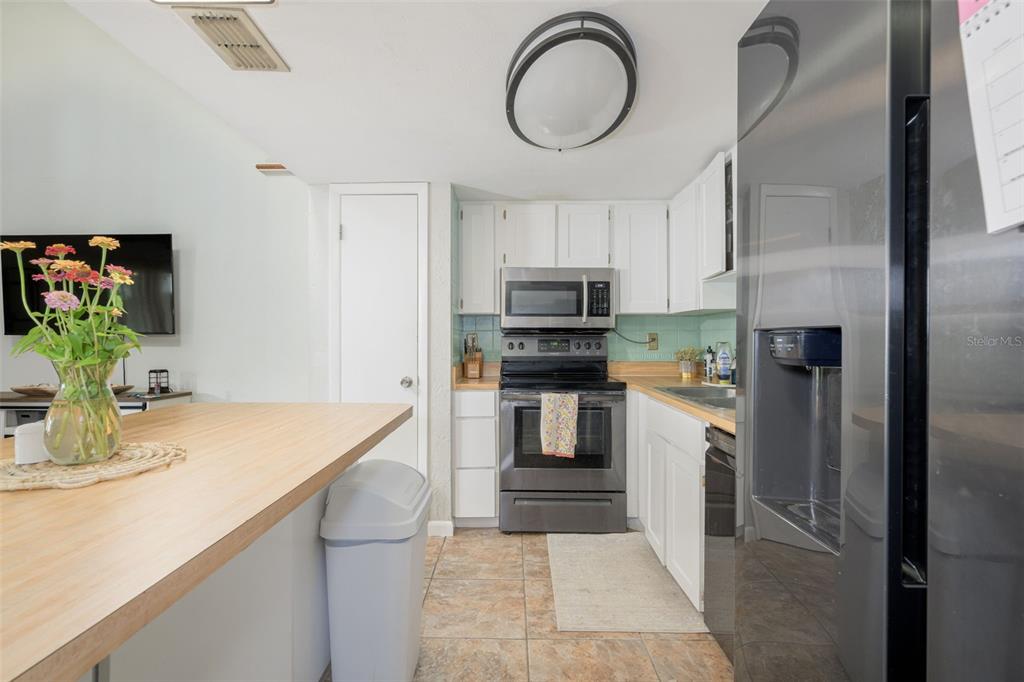 A kitchen features white cabinets, stainless steel appliances, a wood countertop, and tile flooring — 21 OAKWOOD PARK, ORMOND BEACH, FL