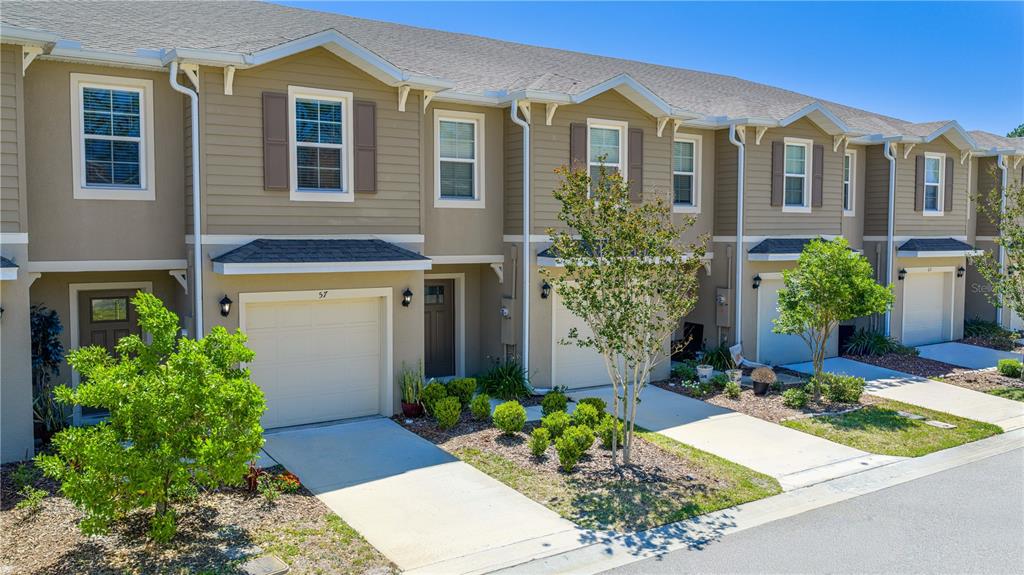 A row of tan townhouses with attached garages and small front yards under a clear sky — 57 BELLA LAGO CIRCLE, PORT ORANGE, FL