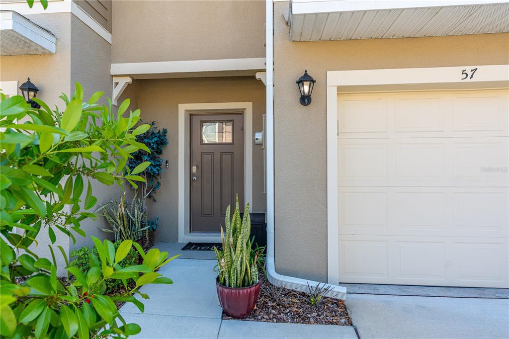 A beige townhouse exterior features a brown front door, a garage, and potted plants — 57 BELLA LAGO CIRCLE, PORT ORANGE, FL