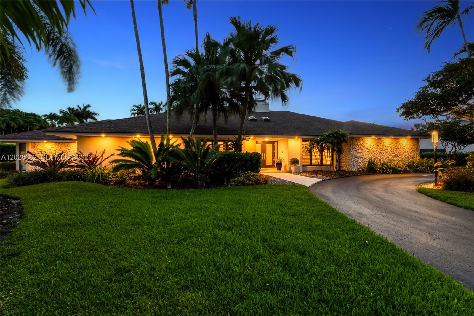 A single-story house with a stone facade, palm trees, and a curved driveway at dusk — 12926 SW 104th Pl, Miami FL 33176, MIAMI, FL