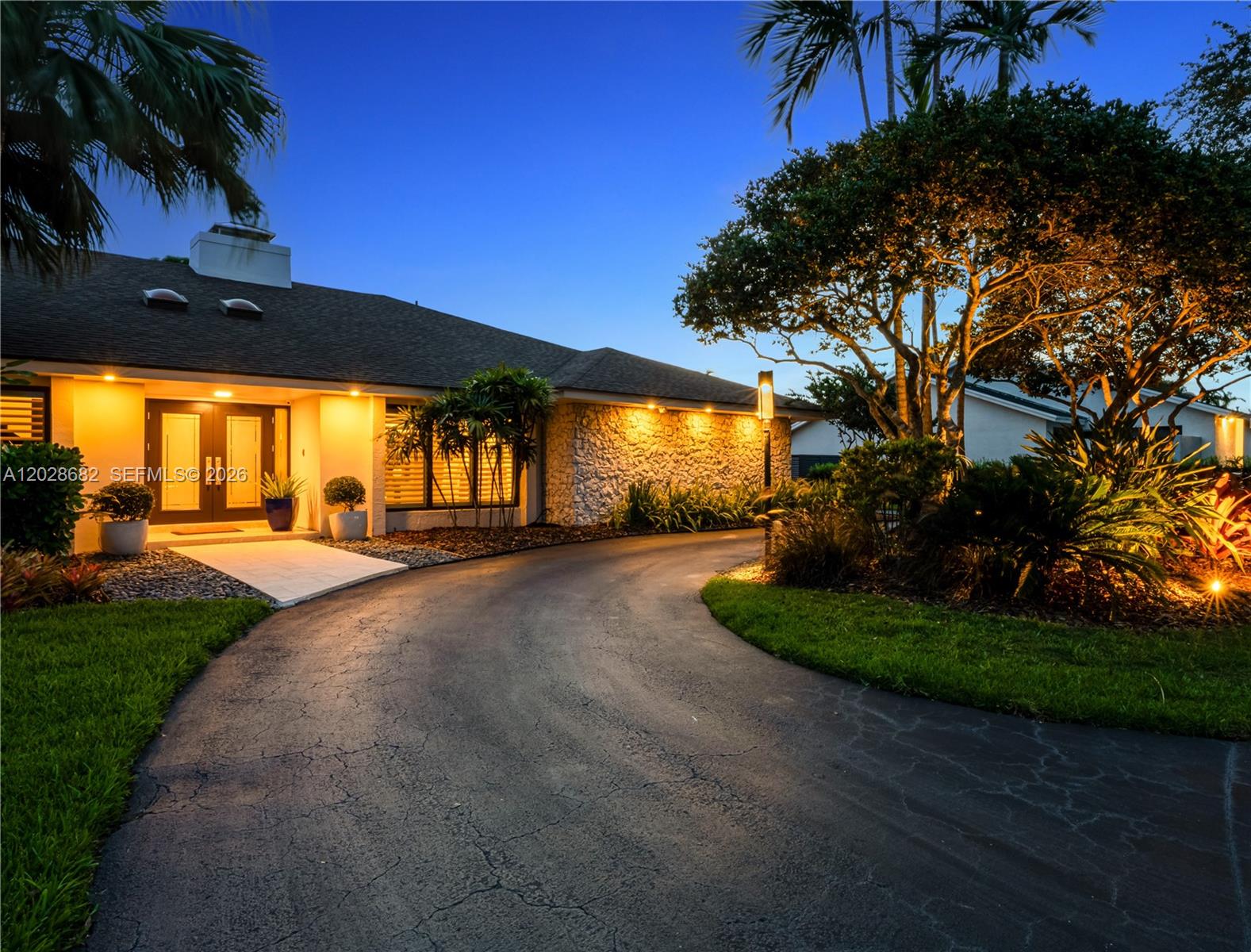 A paved driveway leads to the entrance of a house with stone siding at dusk — 12926 SW 104th Pl, Miami FL 33176, MIAMI, FL