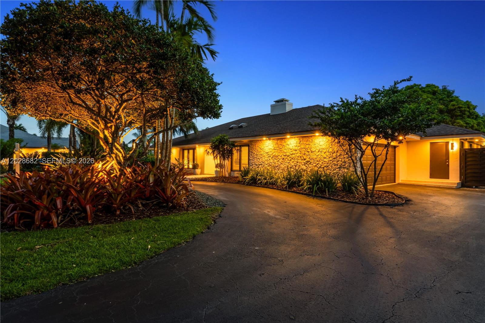 A stone-faced house with a curved driveway and illuminated landscaping at dusk — 12926 SW 104th Pl, Miami FL 33176, MIAMI, FL