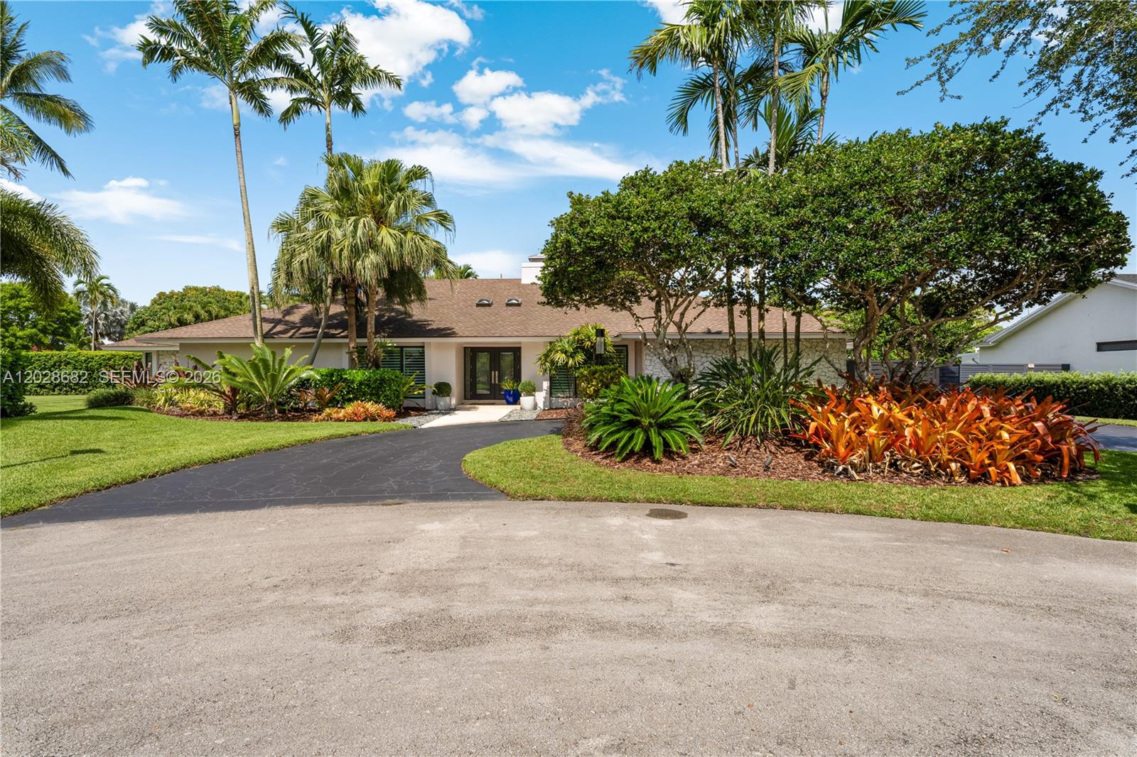 A single-story house features a dark asphalt driveway, lush tropical landscaping, and palm trees — 12926 SW 104th Pl, Miami FL 33176, MIAMI, FL