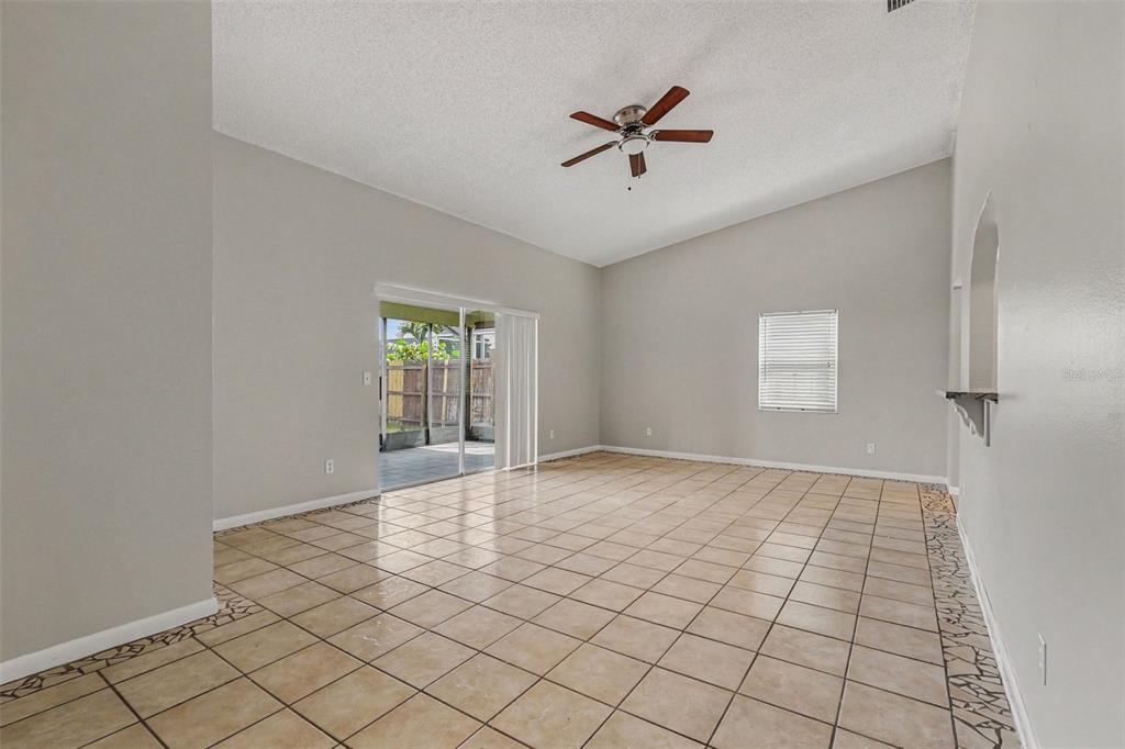 An empty living room with vaulted ceilings, tile flooring, a ceiling fan, and sliding glass doors — 8434 SUN DRIVE, PORT RICHEY, FL