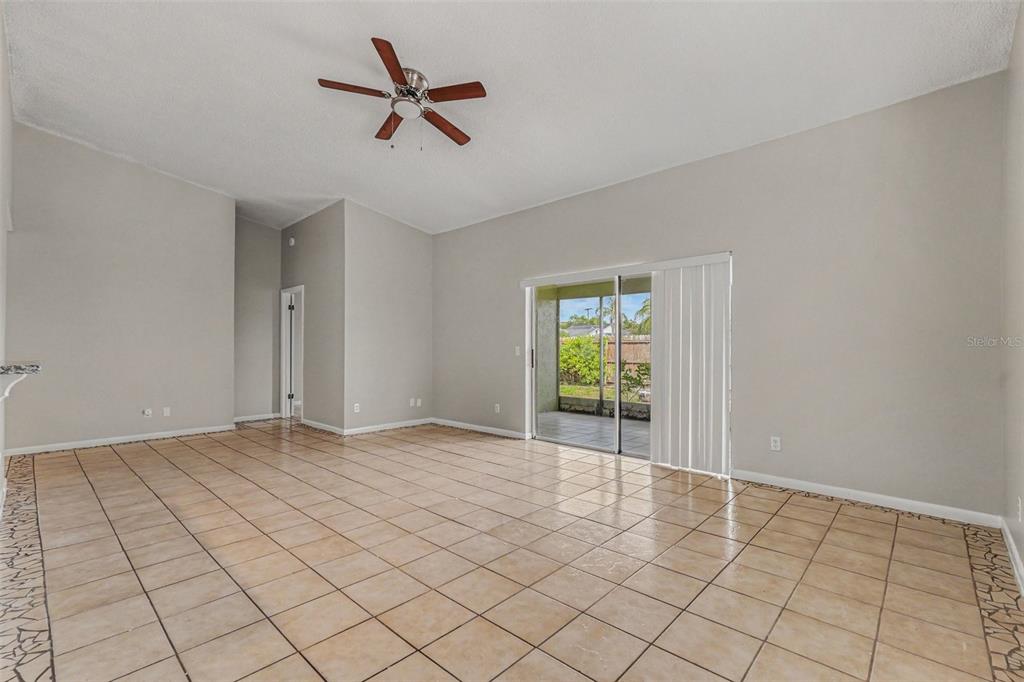 A spacious living room features light-colored tile flooring, neutral walls, a ceiling fan, and sliding doors — 8434 SUN DRIVE, PORT RICHEY, FL