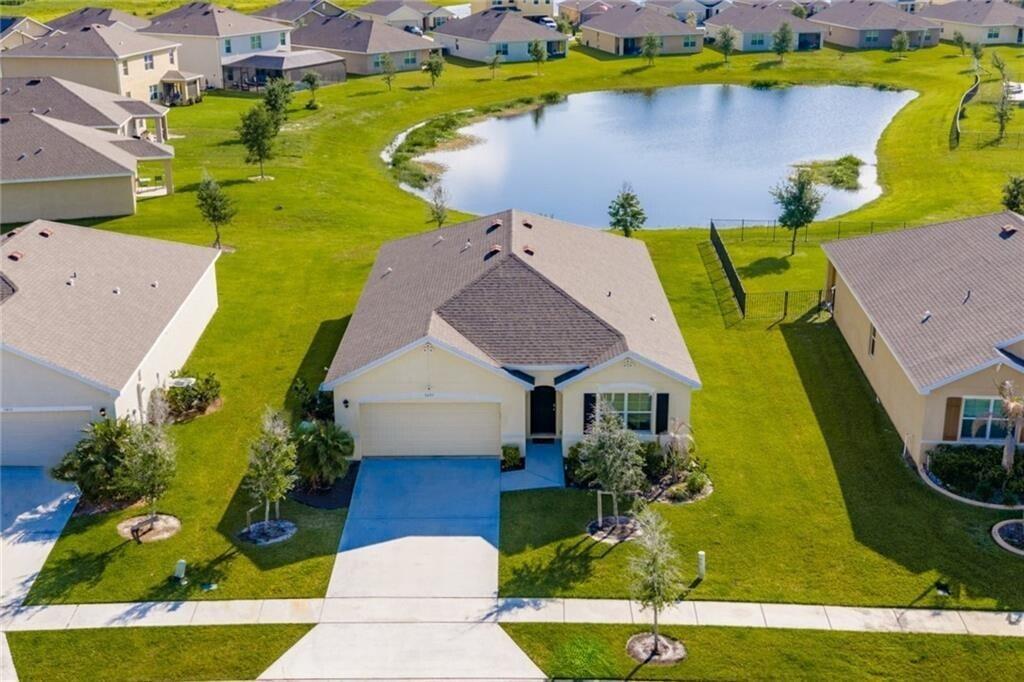 An aerial view of a suburban house with a garage, driveway, and a backyard pond — 3453 Trinity Circle, Fort Pierce FL 34945, FORT PIERCE, FL