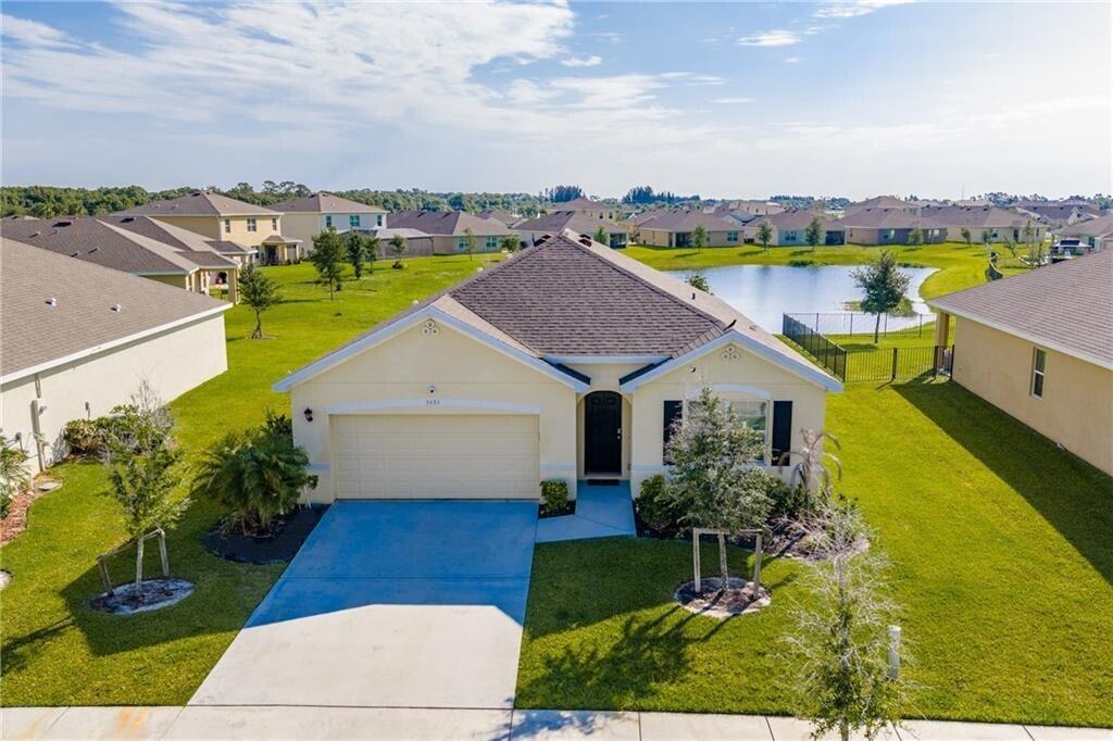 An aerial view of a single-story suburban house with a garage and a backyard pond — 3453 Trinity Circle, Fort Pierce FL 34945, FORT PIERCE, FL
