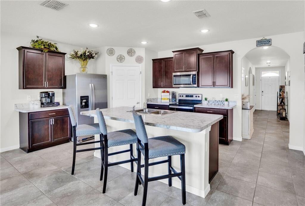 A kitchen features dark wood cabinets, a central island with bar stools, and tiled flooring — 3453 Trinity Circle, Fort Pierce FL 34945, FORT PIERCE, FL