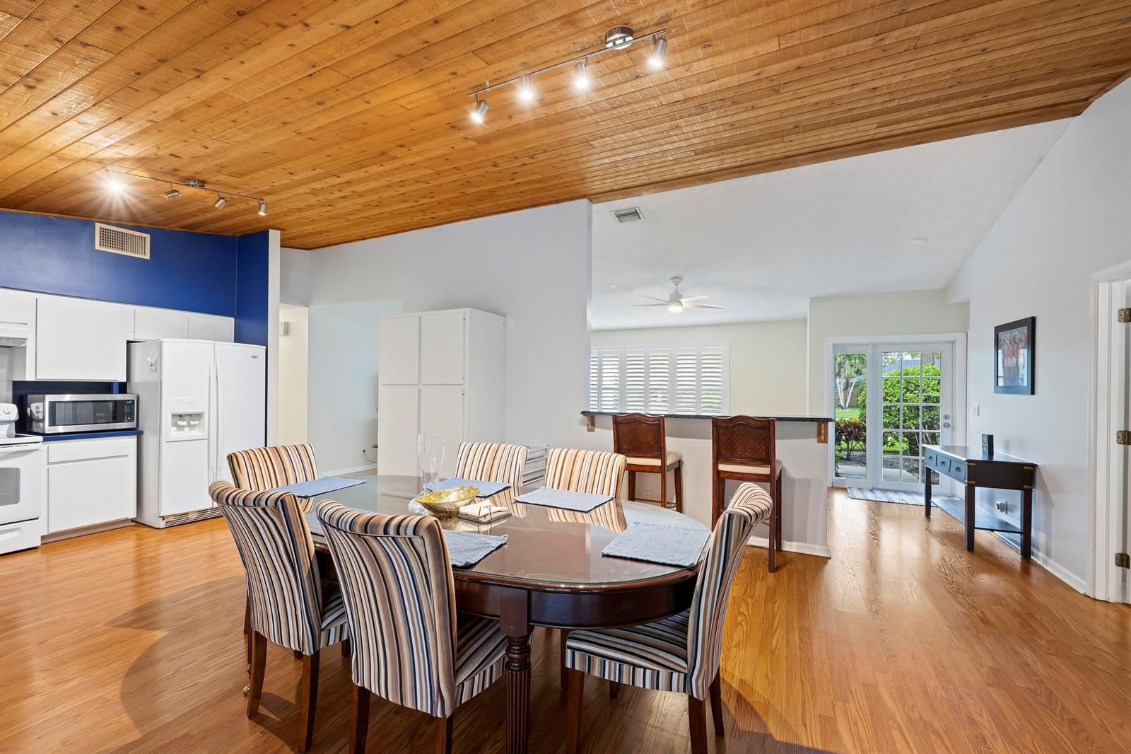 A dining area with a glass table and striped chairs sits beneath a wood-paneled ceiling — 756 Juniper Place, Wellington FL 33414, WELLINGTON, FL