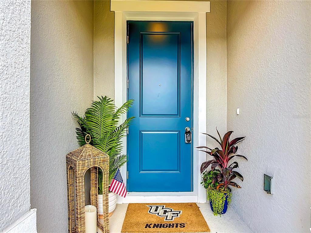 A blue front door with a UCF Knights doormat and potted plants on a porch — 5757 ANDERS WAY, ST CLOUD, FL