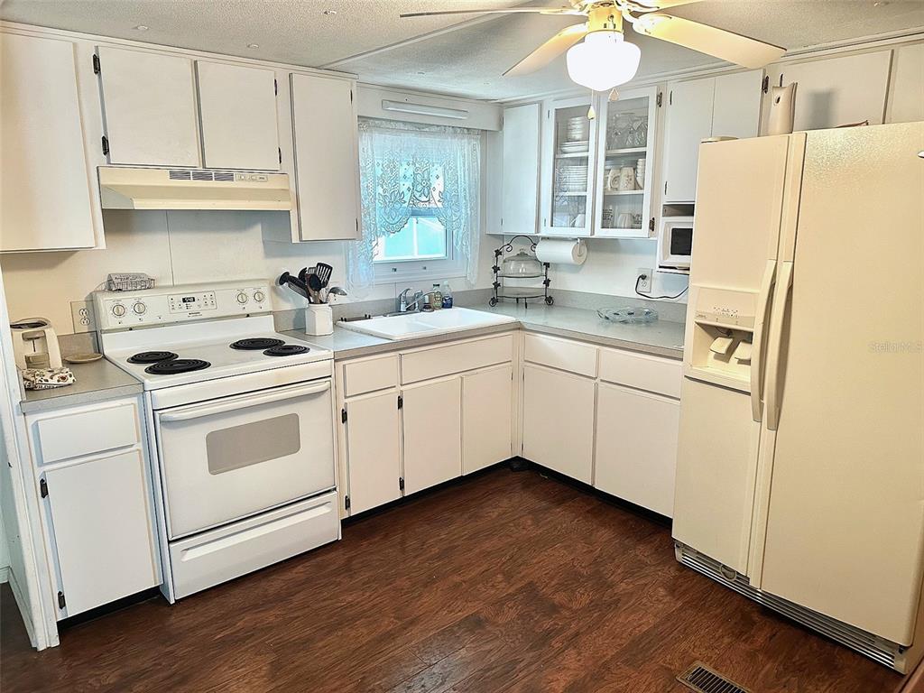 A kitchen features white cabinets, white appliances, a ceiling fan, and dark wood-look flooring — 9790 66TH STREET N UNIT 265, PINELLAS PARK, FL