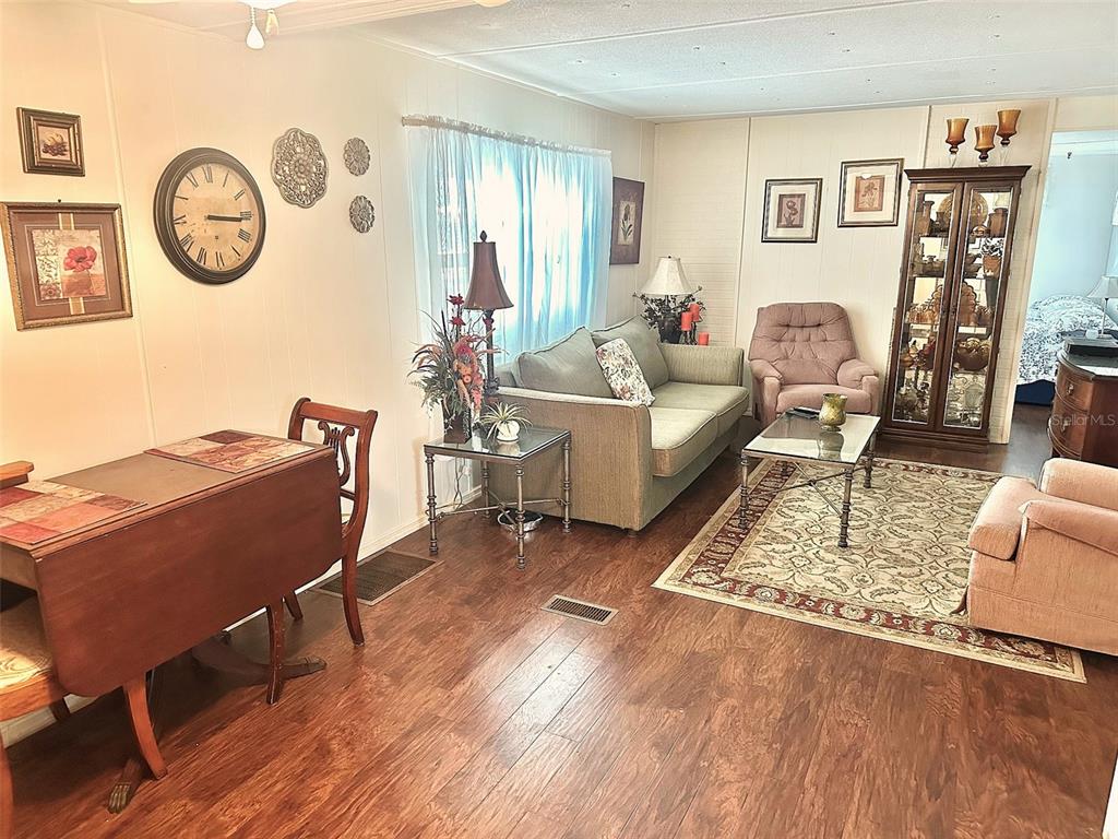 A living room with wood-look flooring, a sofa, armchairs, a dining table, and a display cabinet — 9790 66TH STREET N UNIT 265, PINELLAS PARK, FL
