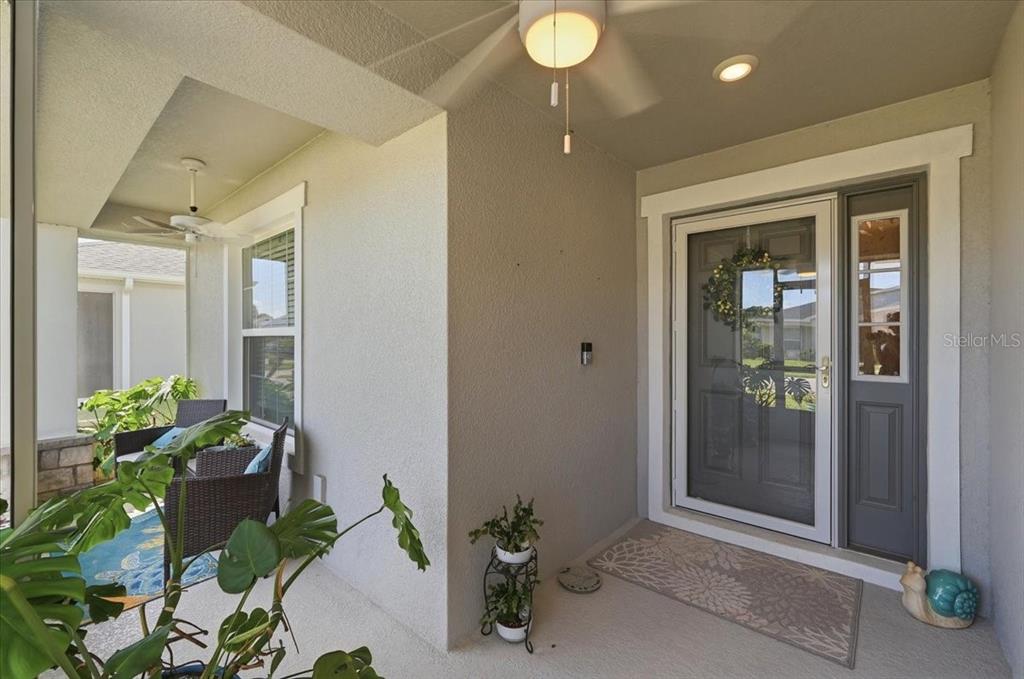 A covered front porch features a ceiling fan, a glass storm door, and potted plants — 2610 SAN MARCO WAY, WINTER HAVEN, FL
