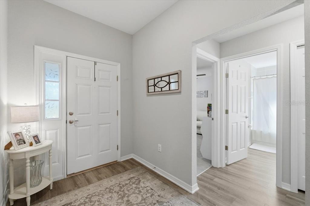 A bright entryway features a white front door, light wood flooring, and a small side table — 2610 SAN MARCO WAY, WINTER HAVEN, FL