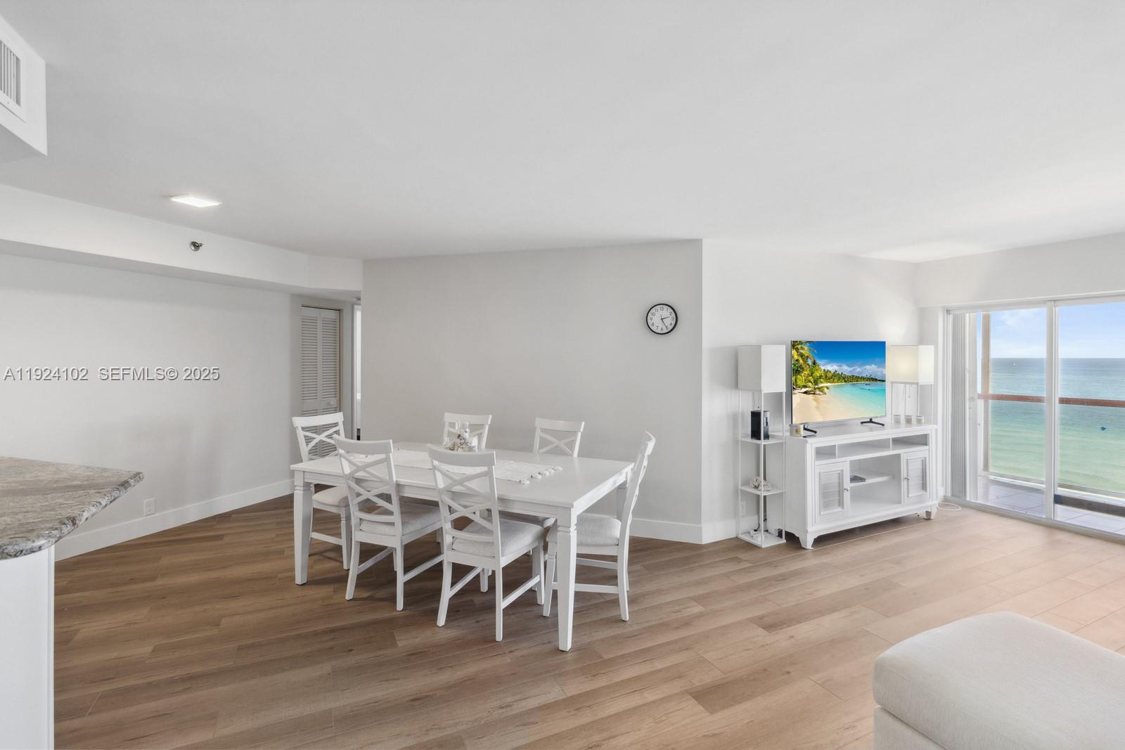 A dining area with a white table and chairs sits next to a living space — 6767 Collins Ave # 909, Miami Beach FL 33141, MIAMI BEACH, FL