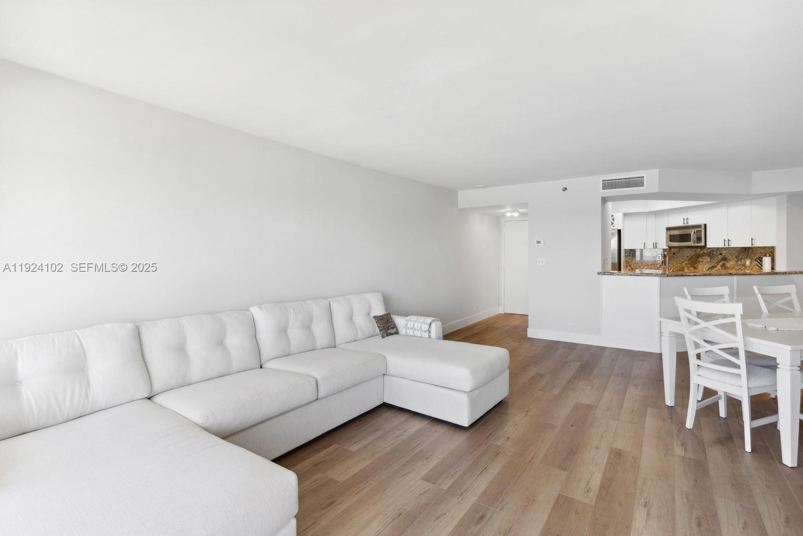 A white sectional sofa sits in a living room with light wood-look flooring — 6767 Collins Ave # 909, Miami Beach FL 33141, MIAMI BEACH, FL