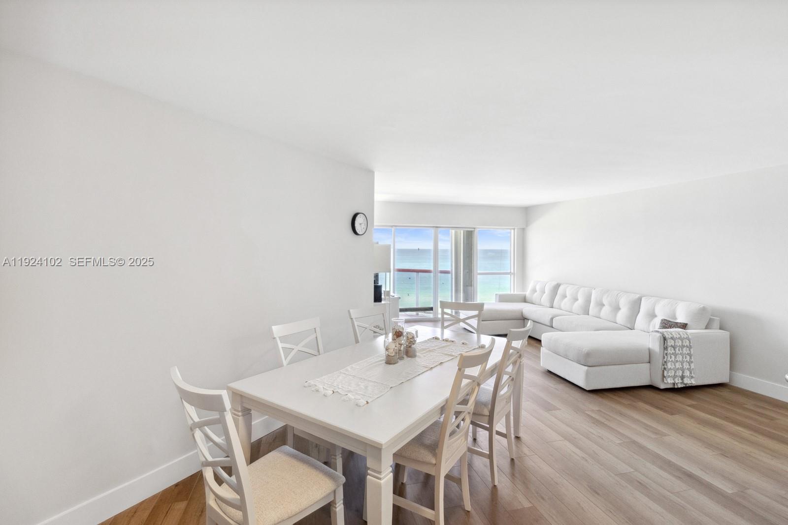 A dining area and living room with white furniture, light wood floors, and ocean views — 6767 Collins Ave # 909, Miami Beach FL 33141, MIAMI BEACH, FL