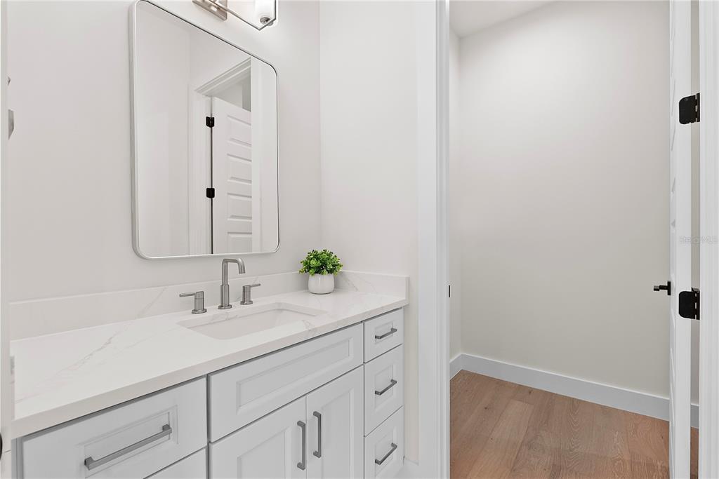 A modern bathroom features a white vanity with marble countertop, rectangular mirror, and wood flooring — 2505 AMHERST AVENUE, ORLANDO, FL