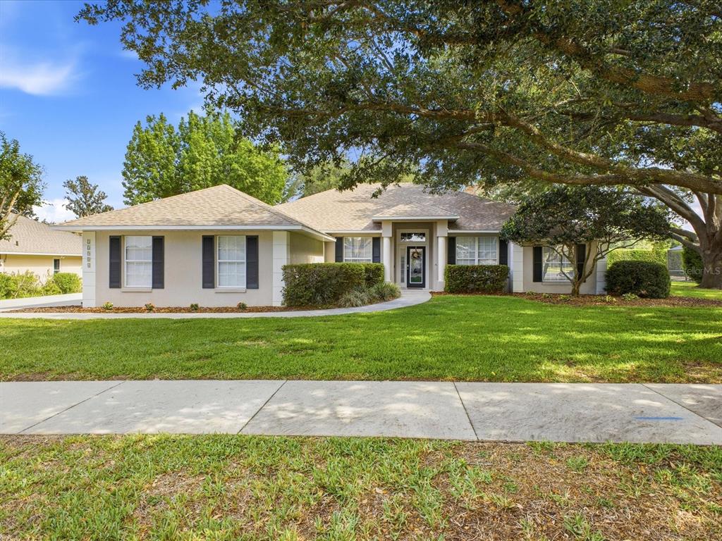 A single-story house with a beige exterior, dark shutters, and a large tree in front — 11906 GRACES WAY, CLERMONT, FL