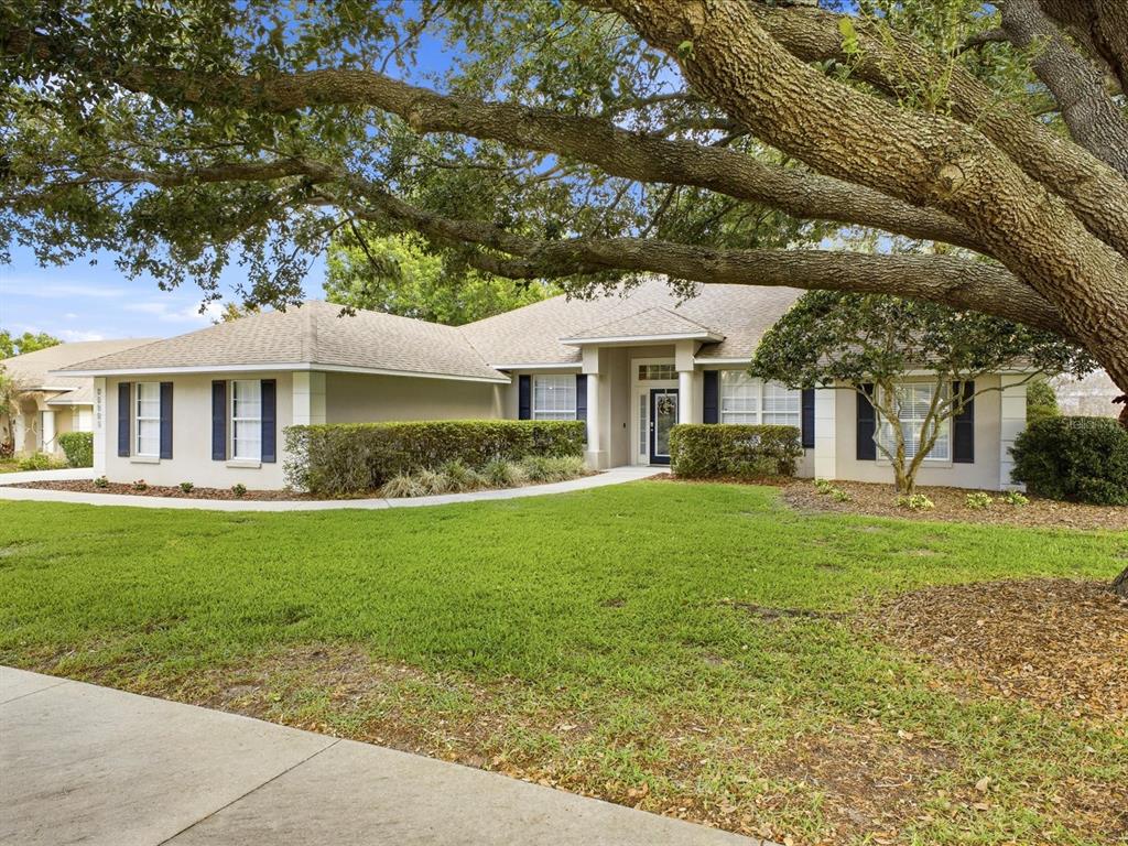 A single-story house with a beige exterior, dark shutters, and a large tree in front — 11906 GRACES WAY, CLERMONT, FL