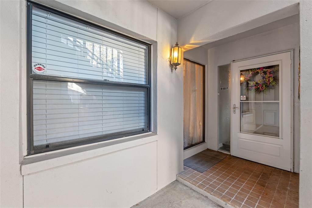 A white exterior entryway features a window with blinds, a storm door, and tile flooring — 300 S FLORIDA AVENUE UNIT 600F, TARPON SPRINGS, FL