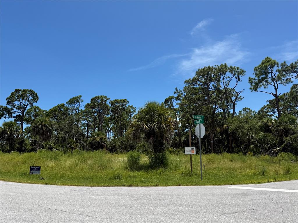 A vacant, grassy corner lot features a street sign and a for sale sign — 109 HAWK DRIVE, ROTONDA WEST, FL