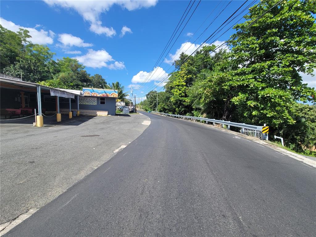 A paved road curves past a small commercial building with a covered outdoor seating area — CARR 829, KM 2.3 BO. BUENA VISTA, BAYAMON, PR