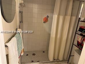 A tiled walk-in shower features a grab bar, a patterned floor, and a beige curtain — 3571 Inverrary Dr # 408, Lauderhill FL 33319, LAUDERHILL, FL