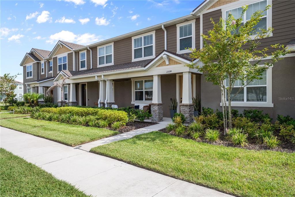 A two-story townhouse exterior features brown siding, stone-accented columns, and a front walkway — 11574 BUOY POINT PLACE, ORLANDO, FL