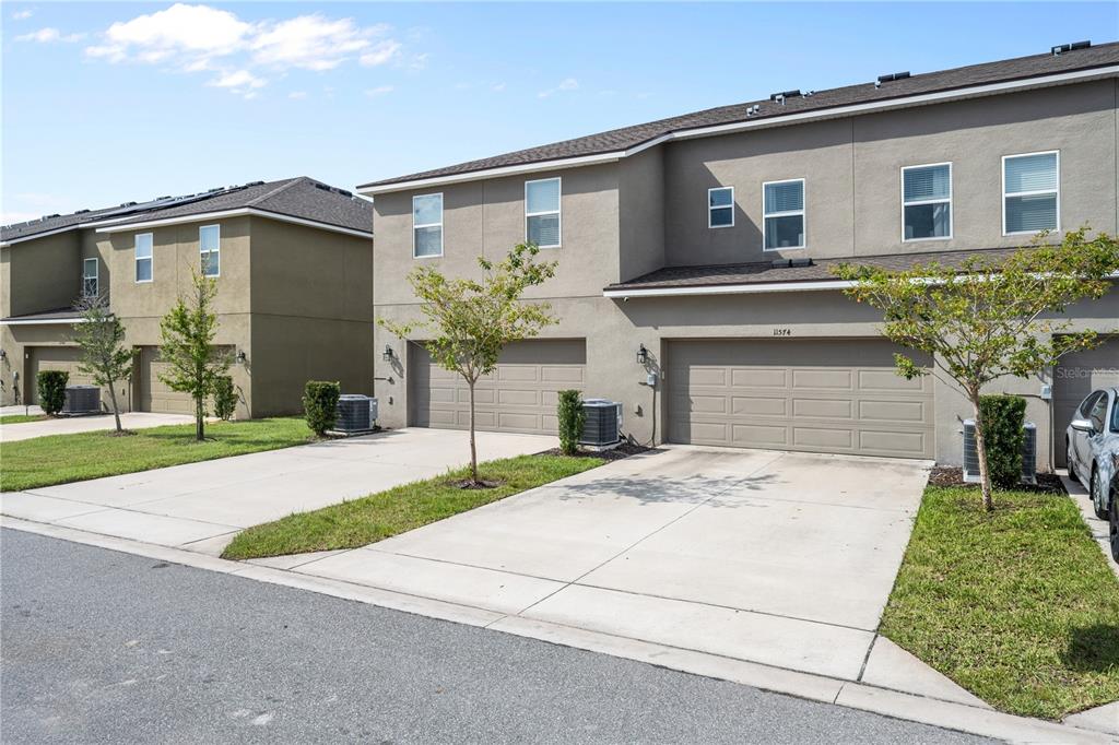 A view of the exterior of two attached townhomes with concrete driveways and garages — 11574 BUOY POINT PLACE, ORLANDO, FL
