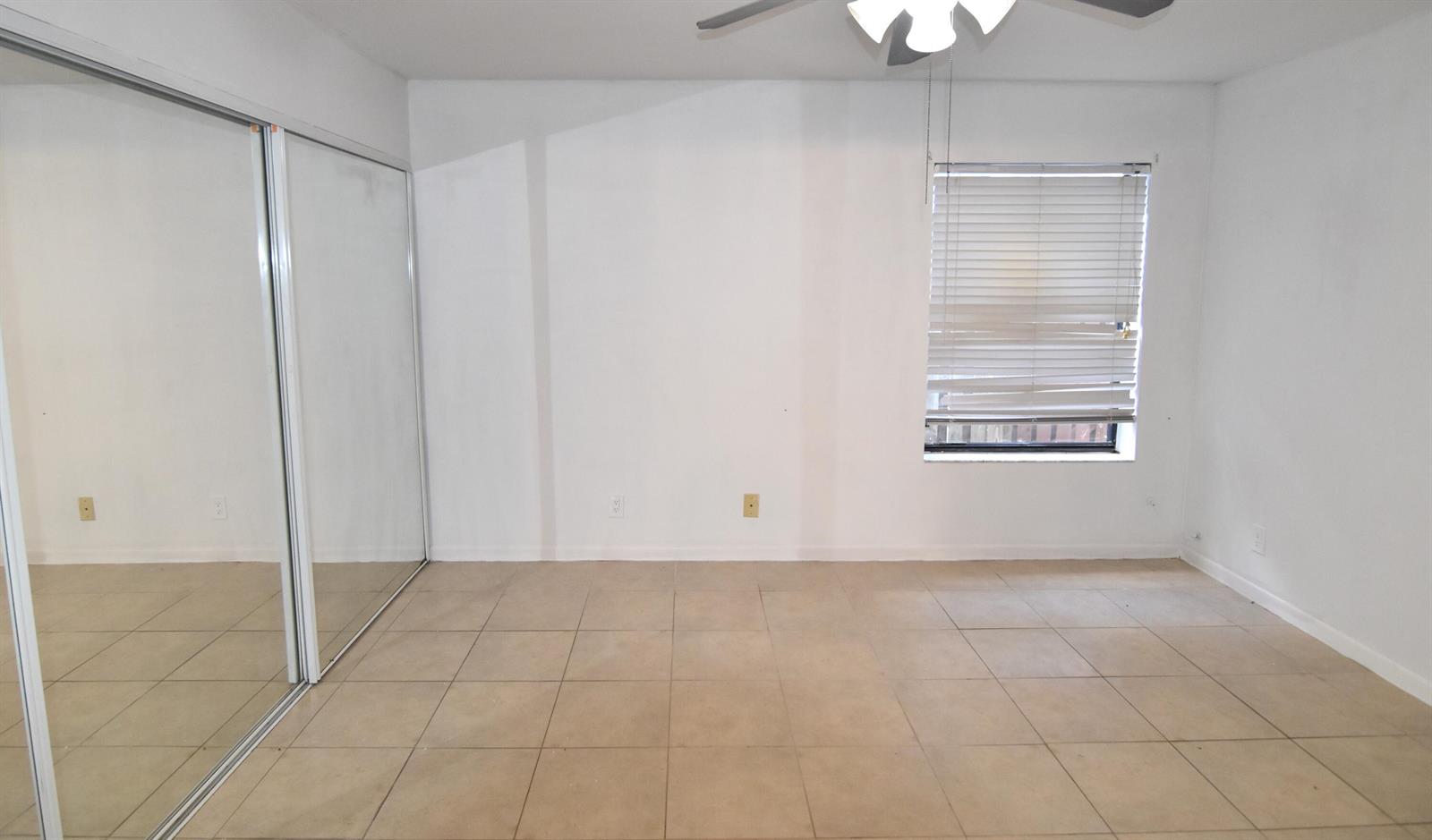 An empty bedroom features white walls, beige tile flooring, a mirrored closet, and a window — 3 Crossings Circle # B, Boynton Beach FL 33435, BOYNTON BEACH, FL