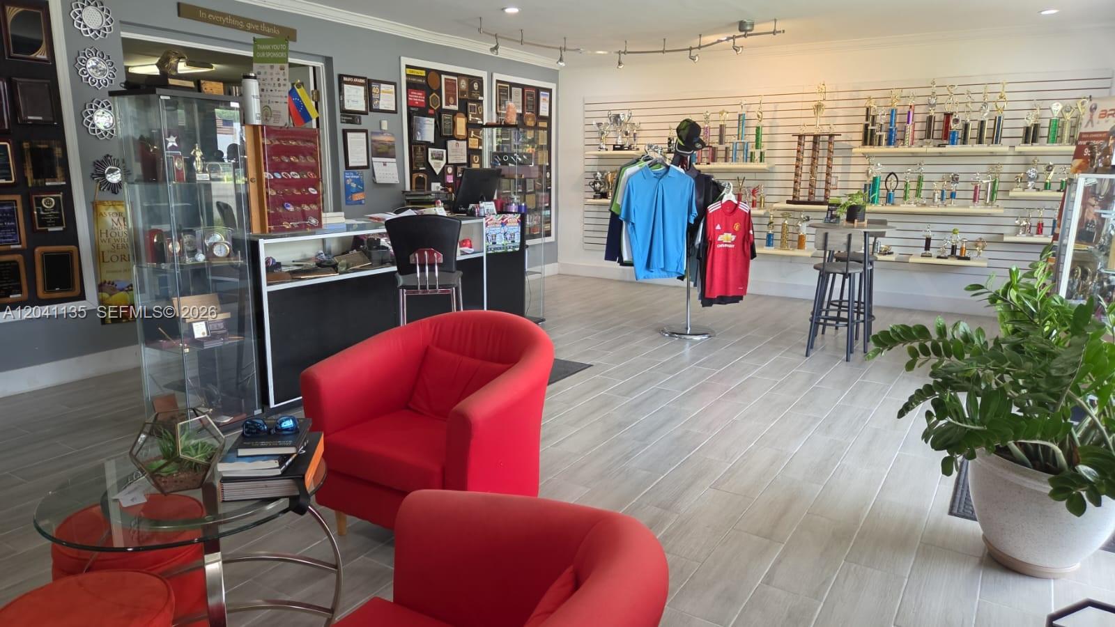 A retail space features trophy displays, clothing racks, red armchairs, and light wood-look flooring — 5824 Johnson St, Hollywood FL 33021, HOLLYWOOD, FL