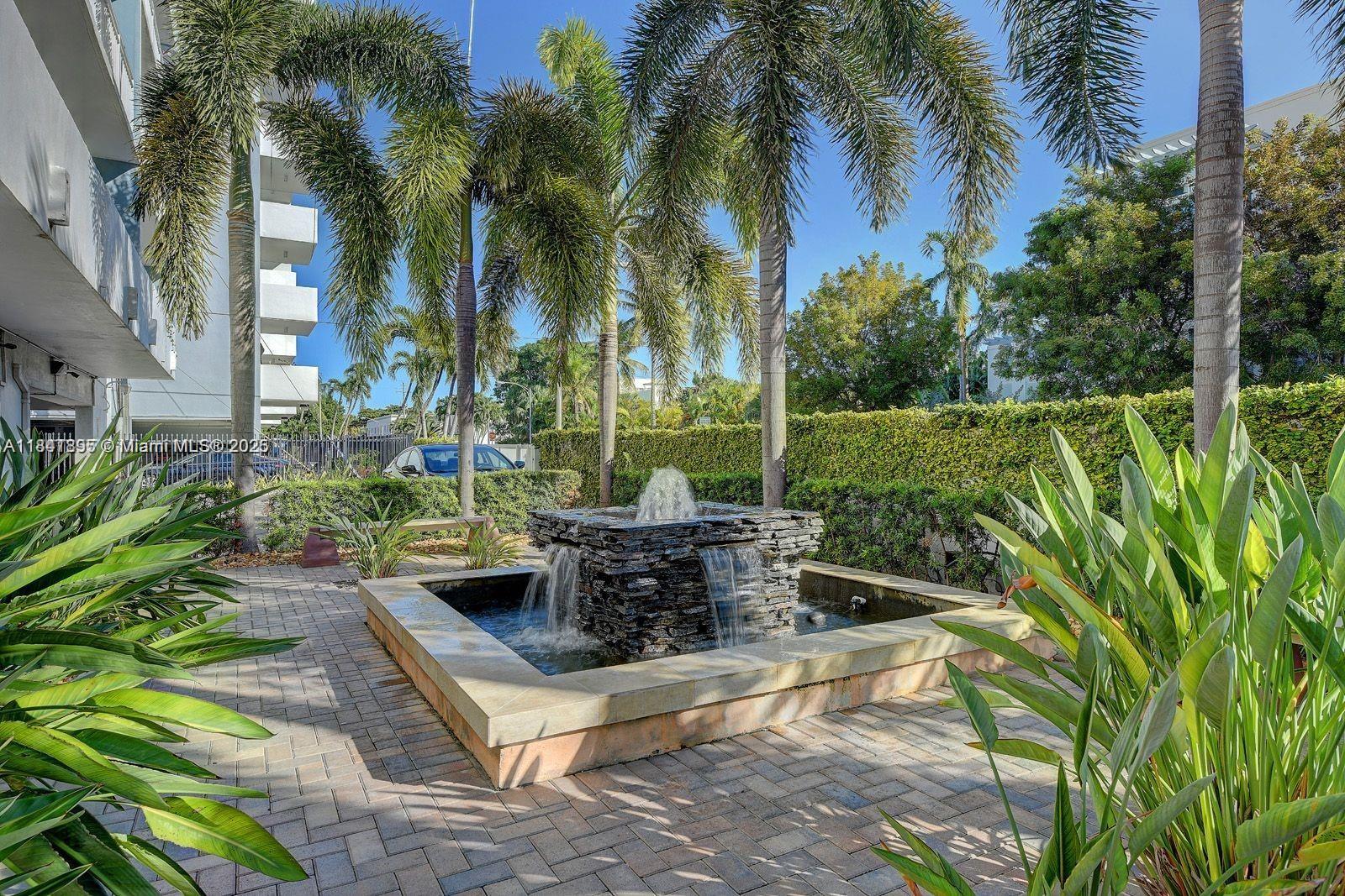 A stone fountain sits in a paved courtyard surrounded by palm trees and a hedge — 1045 10th St # 907, Miami Beach FL 33139, MIAMI BEACH, FL