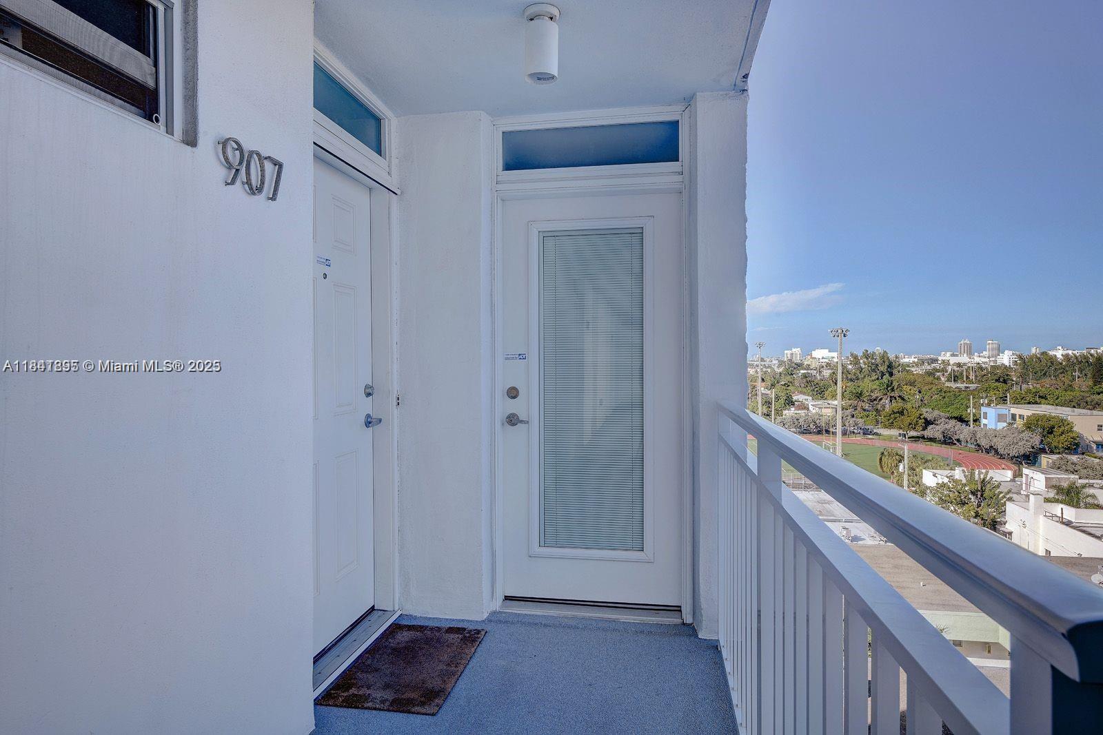An outdoor balcony features two white doors, a gray floor, and a metal railing — 1045 10th St # 907, Miami Beach FL 33139, MIAMI BEACH, FL