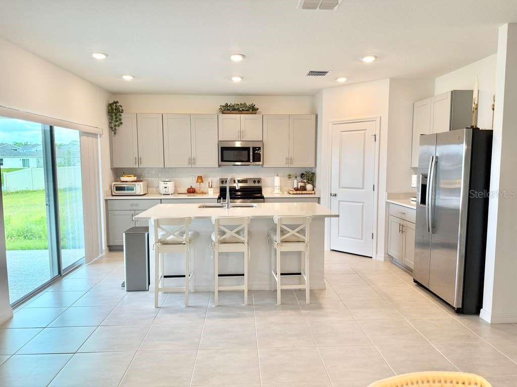 A kitchen with light gray cabinets, stainless steel appliances, a center island, and tile flooring — 4773 YELLOW ELDER WAY, KISSIMMEE, FL