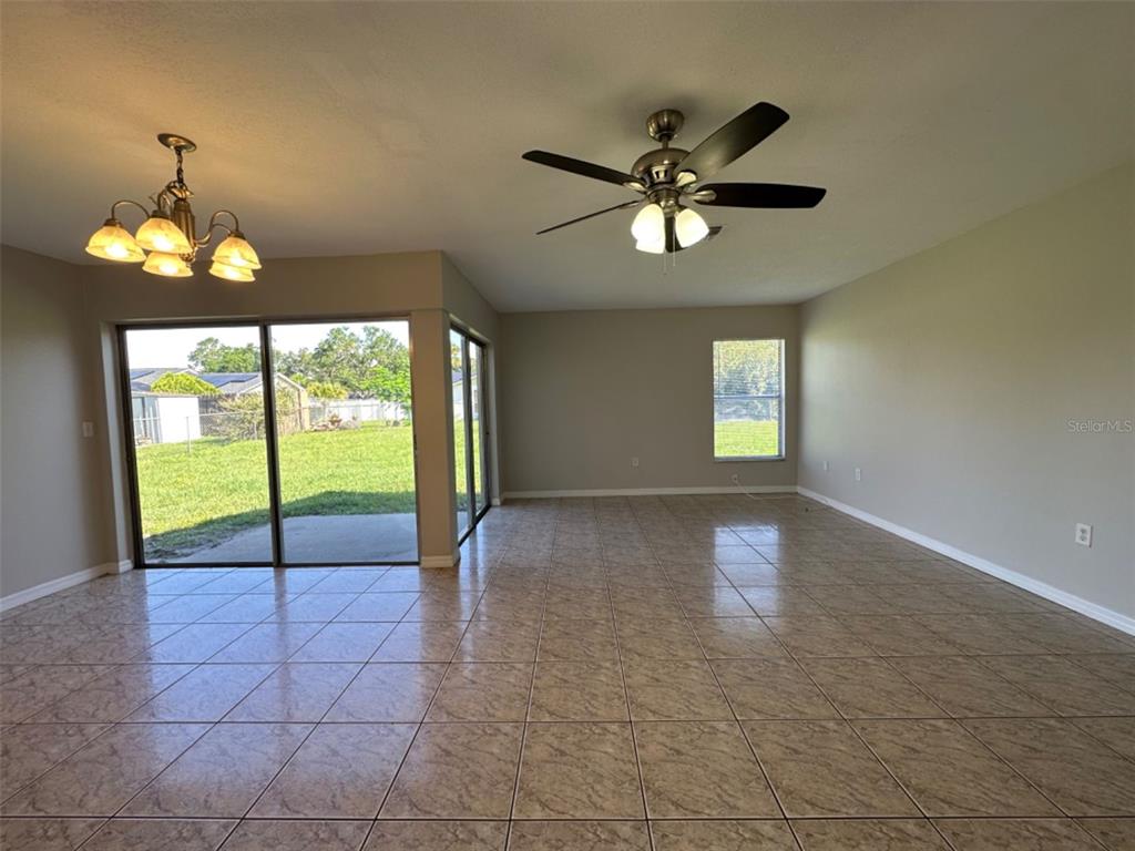 An open living area with beige tile floors, a ceiling fan, and sliding glass doors — 707 WEDGE LANE, POINCIANA, FL