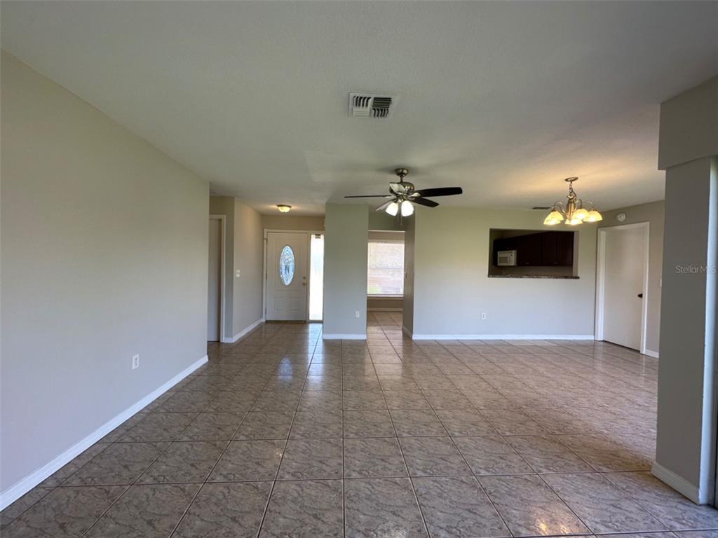 An open-concept living area features beige tile flooring, neutral walls, a ceiling fan, and chandelier — 707 WEDGE LANE, POINCIANA, FL