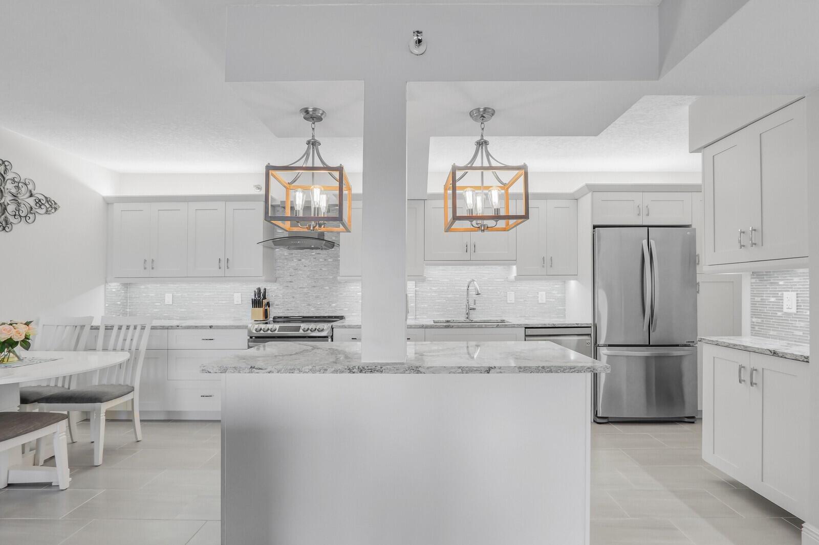 A modern white kitchen features a central island, stainless steel appliances, and two pendant lights — 4444 NE Ocean Boulevard # E2, Jensen Beach FL 34957, JENSEN BEACH, FL