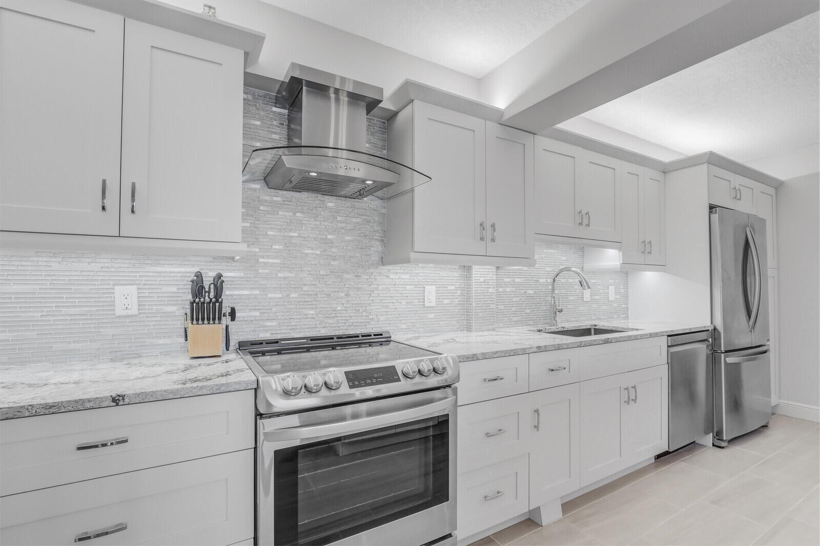 A modern kitchen features light gray cabinets, stainless steel appliances, and a tiled backsplash — 4444 NE Ocean Boulevard # E2, Jensen Beach FL 34957, JENSEN BEACH, FL
