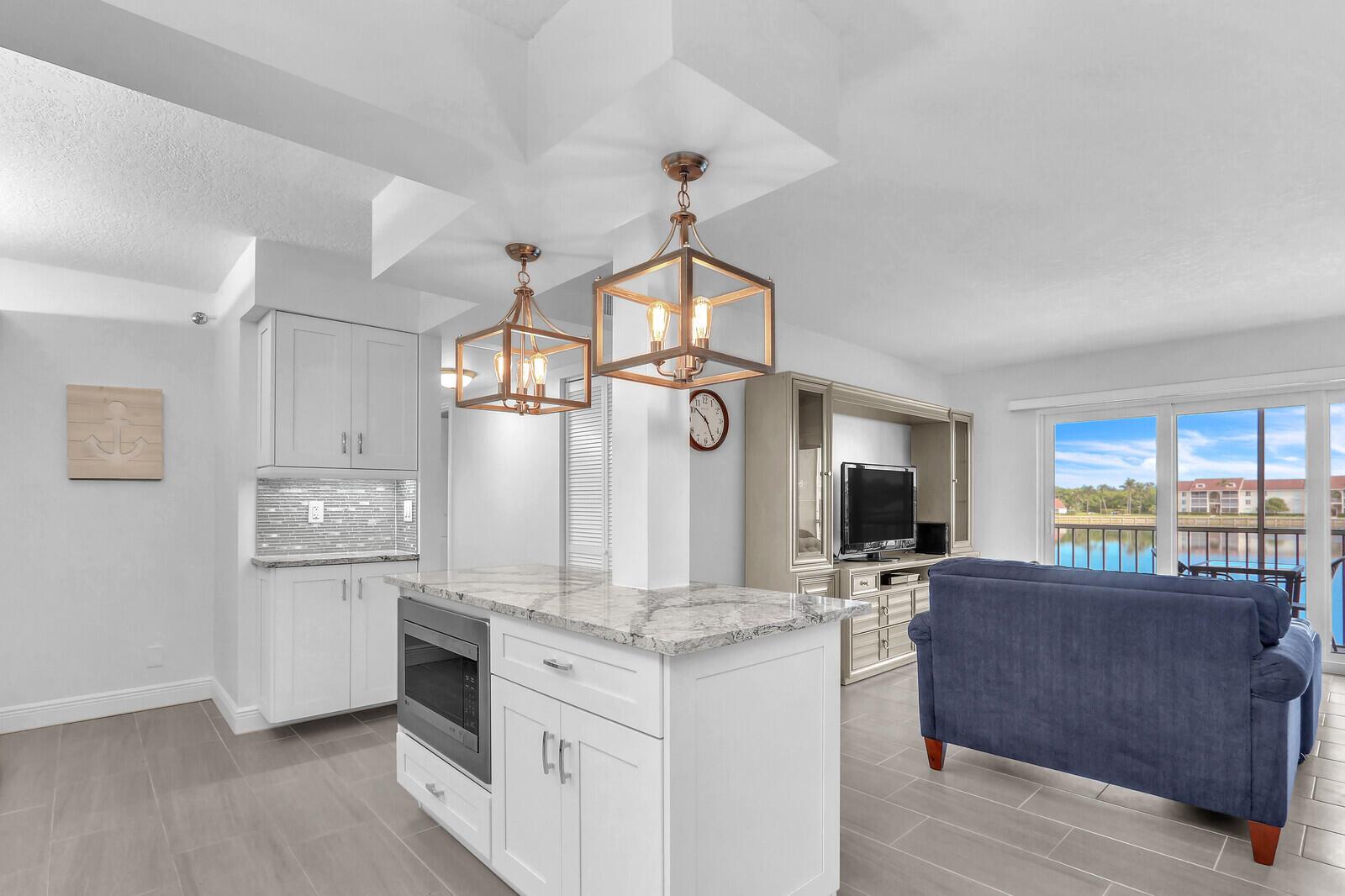 A kitchen with white cabinets and a marble island overlooks a living area with water views — 4444 NE Ocean Boulevard # E2, Jensen Beach FL 34957, JENSEN BEACH, FL