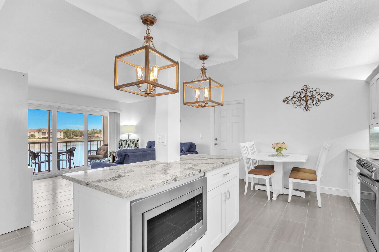 A kitchen with a white island, granite countertops, and pendant lights overlooking a living area — 4444 NE Ocean Boulevard # E2, Jensen Beach FL 34957, JENSEN BEACH, FL