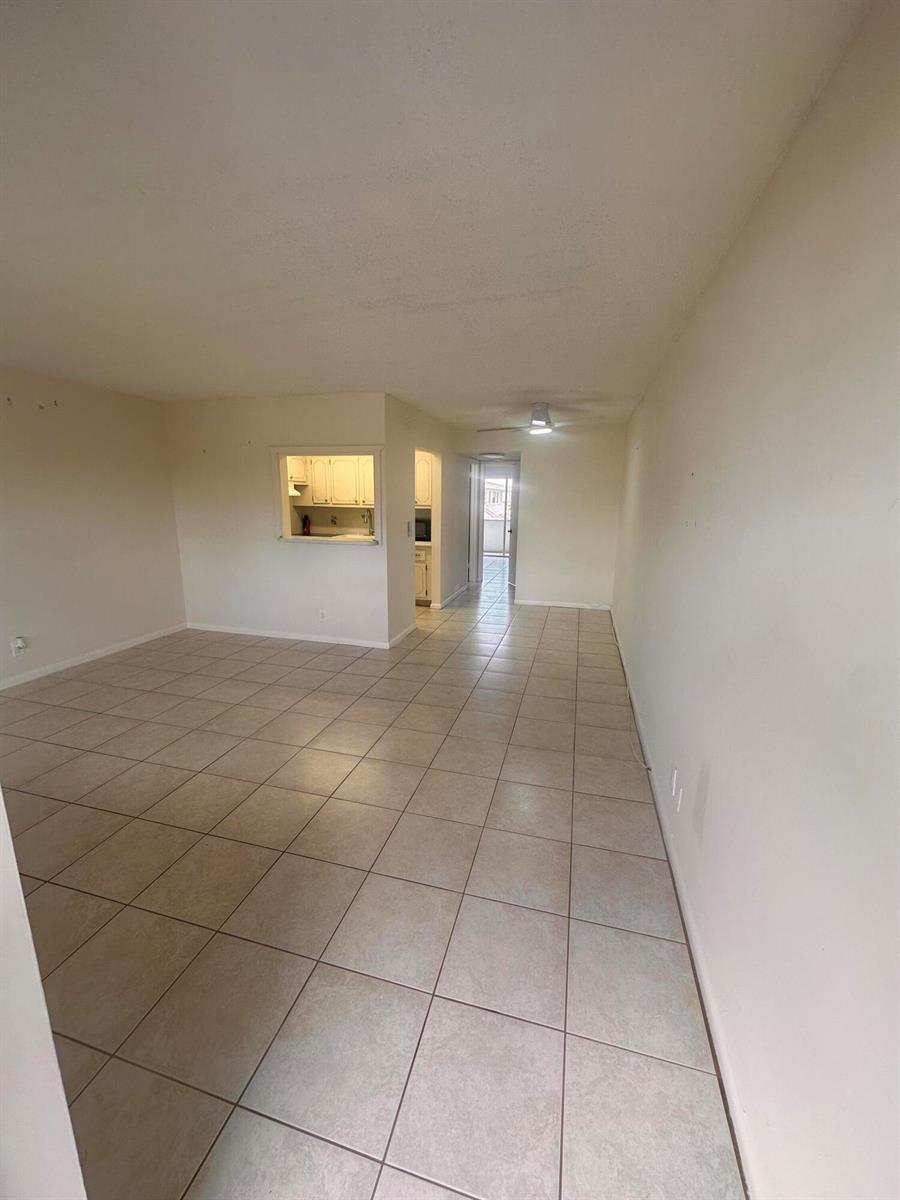An empty living area features beige tile flooring, white walls, and a kitchen pass-through window — 39 Cambridge B, West Palm Beach FL 33417, WEST PALM BEACH, FL