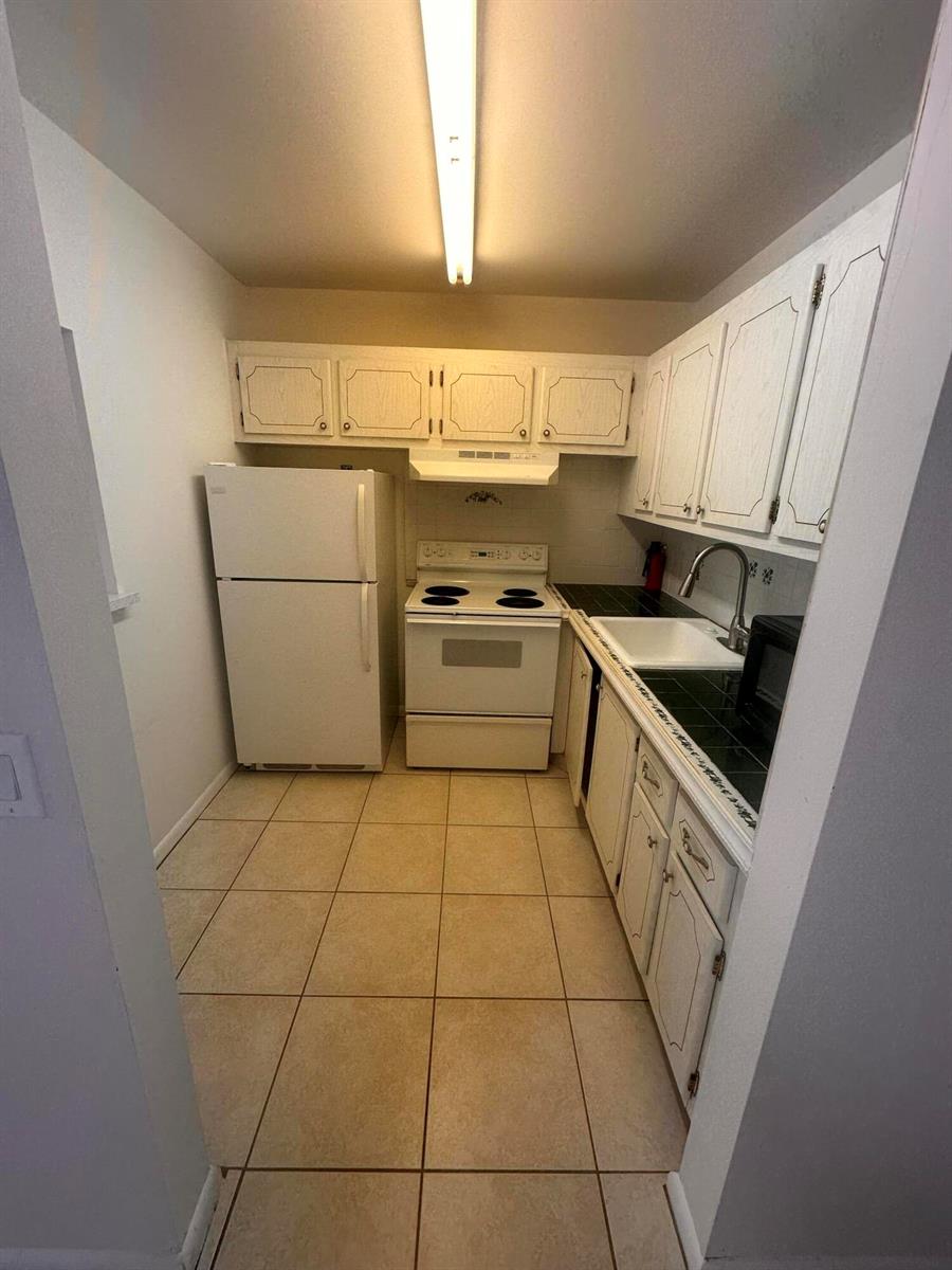 A galley kitchen features white cabinets, a white stove, a refrigerator, and tiled countertops — 39 Cambridge B, West Palm Beach FL 33417, WEST PALM BEACH, FL
