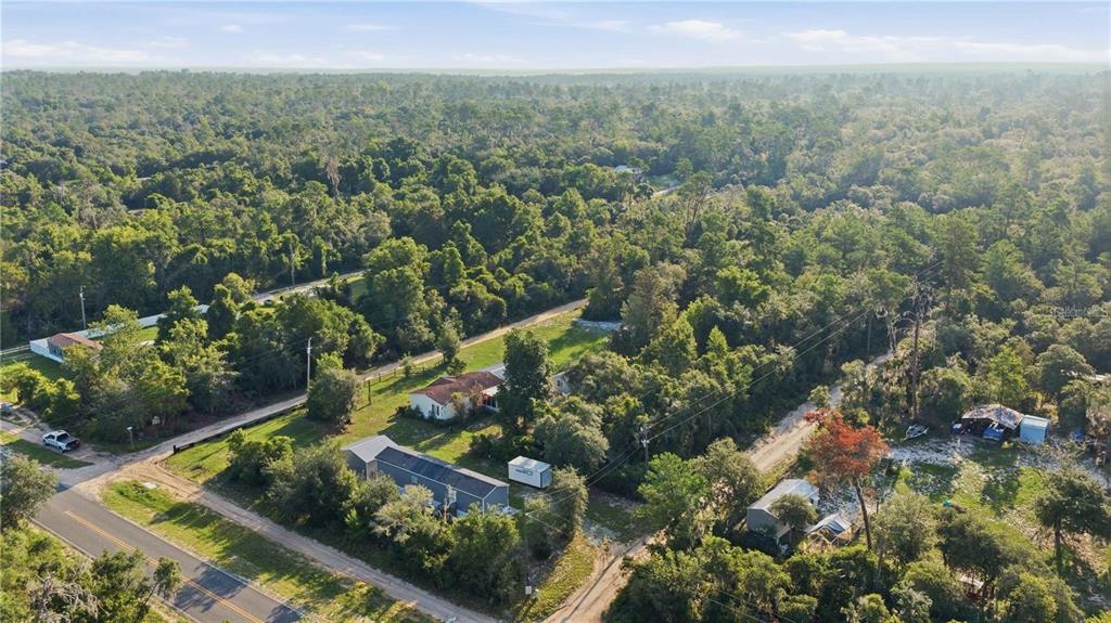 An aerial view shows a house and outbuildings surrounded by dense forest and a road — TBD NE 235TH STREET, FORT MC COY, FL