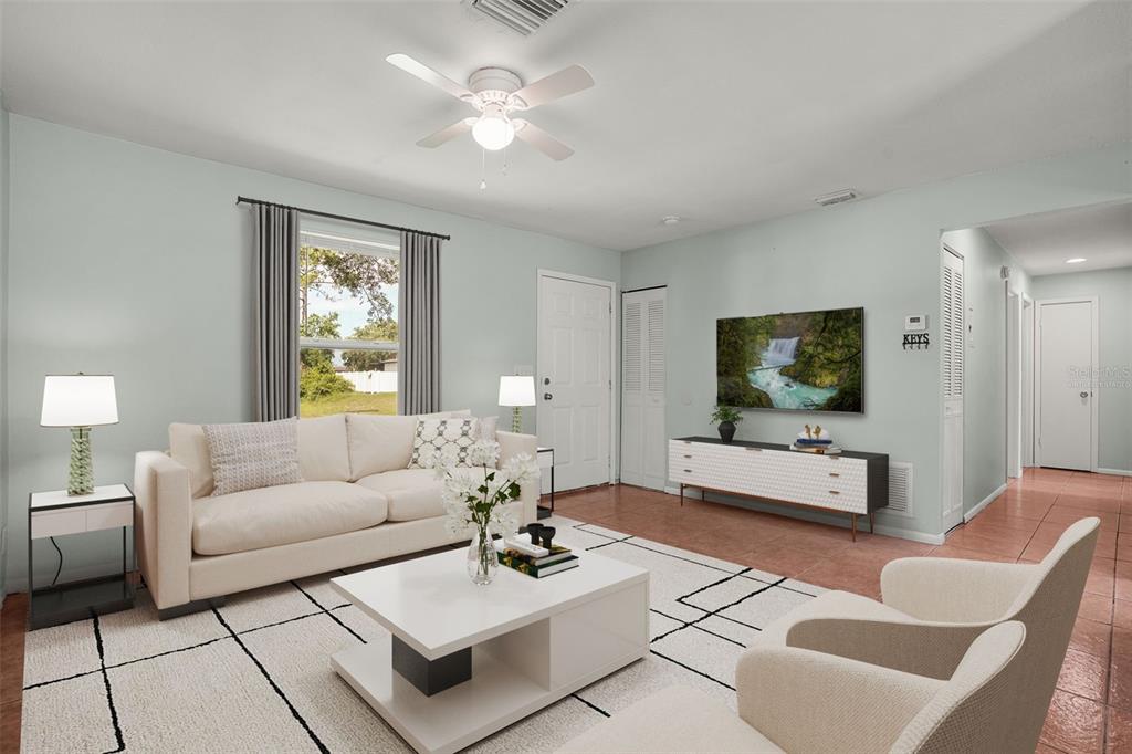 A living room features a white sofa, a coffee table, and a wall-mounted television — 1067 LYRIC DRIVE, DELTONA, FL