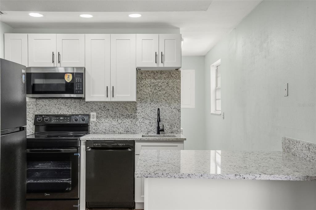 A kitchen with white cabinets, granite countertops, and black appliances — 1067 LYRIC DRIVE, DELTONA, FL