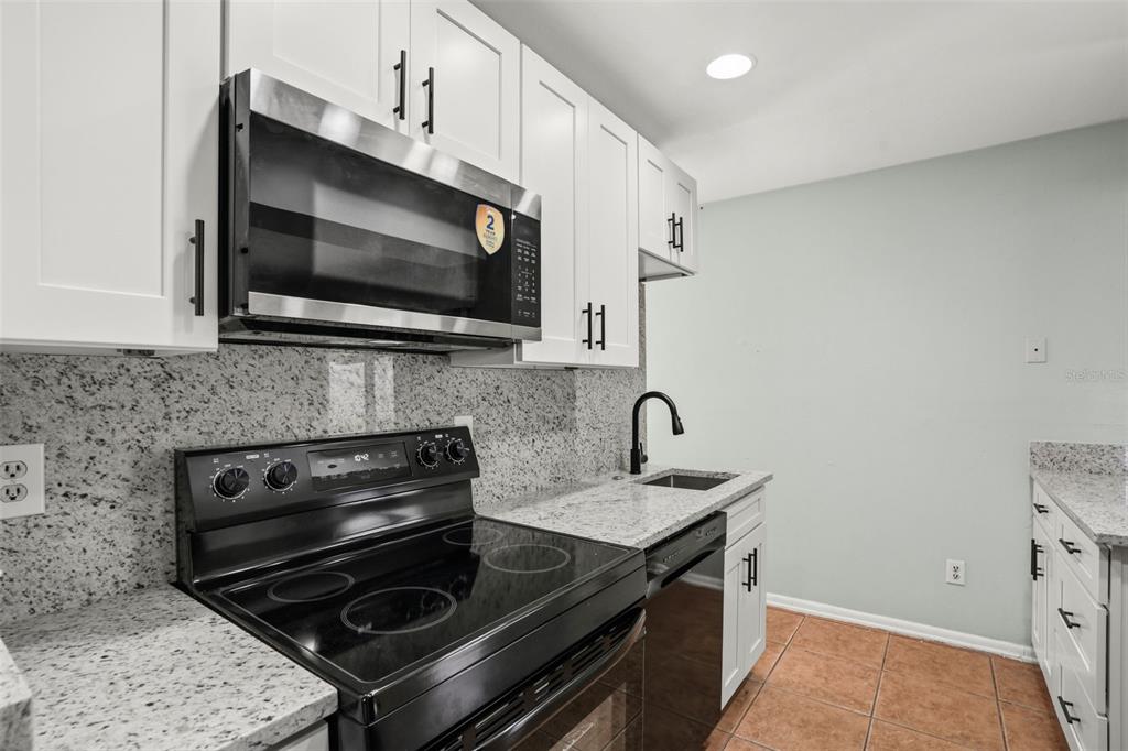 A kitchen features white cabinets, granite countertops, a black stove, and a stainless steel microwave — 1067 LYRIC DRIVE, DELTONA, FL