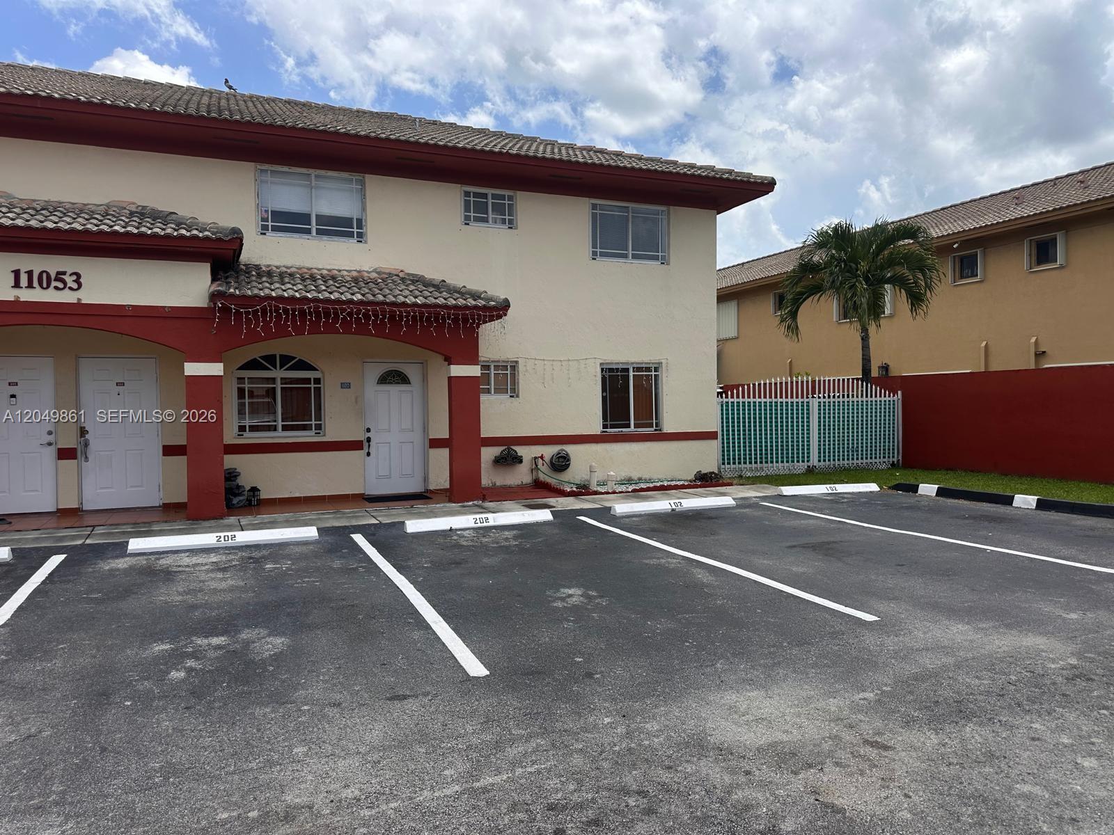 A two-story residential building features a red-trimmed entrance and assigned parking spaces in front — 11053 W Okeechobee Rd # 102, Hialeah Gardens FL 33018, HIALEAH GARDENS, FL