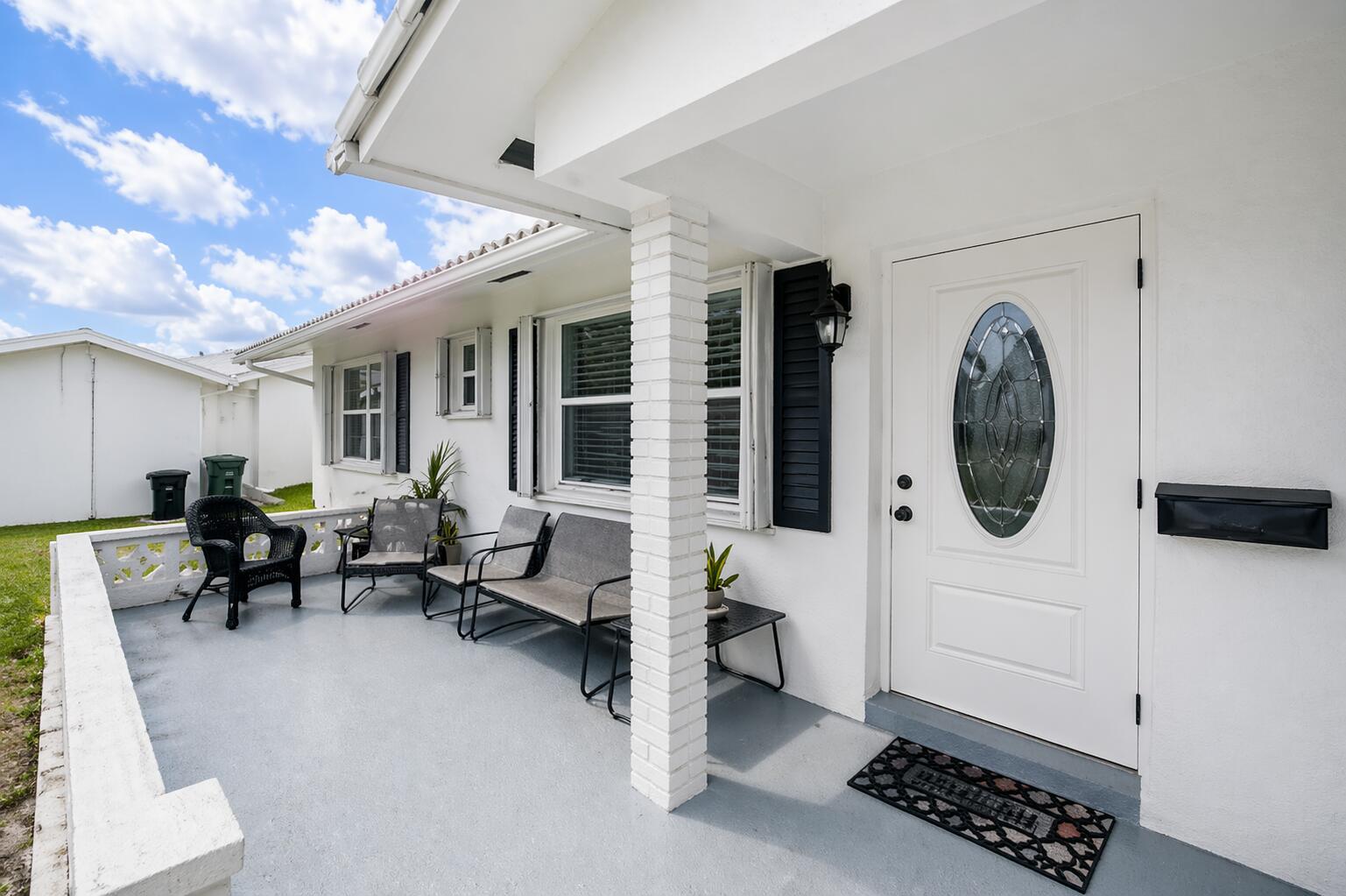 A white house exterior features a covered porch with grey flooring and black patio furniture — 517 SW 18th Street, Boynton Beach FL 33426, BOYNTON BEACH, FL
