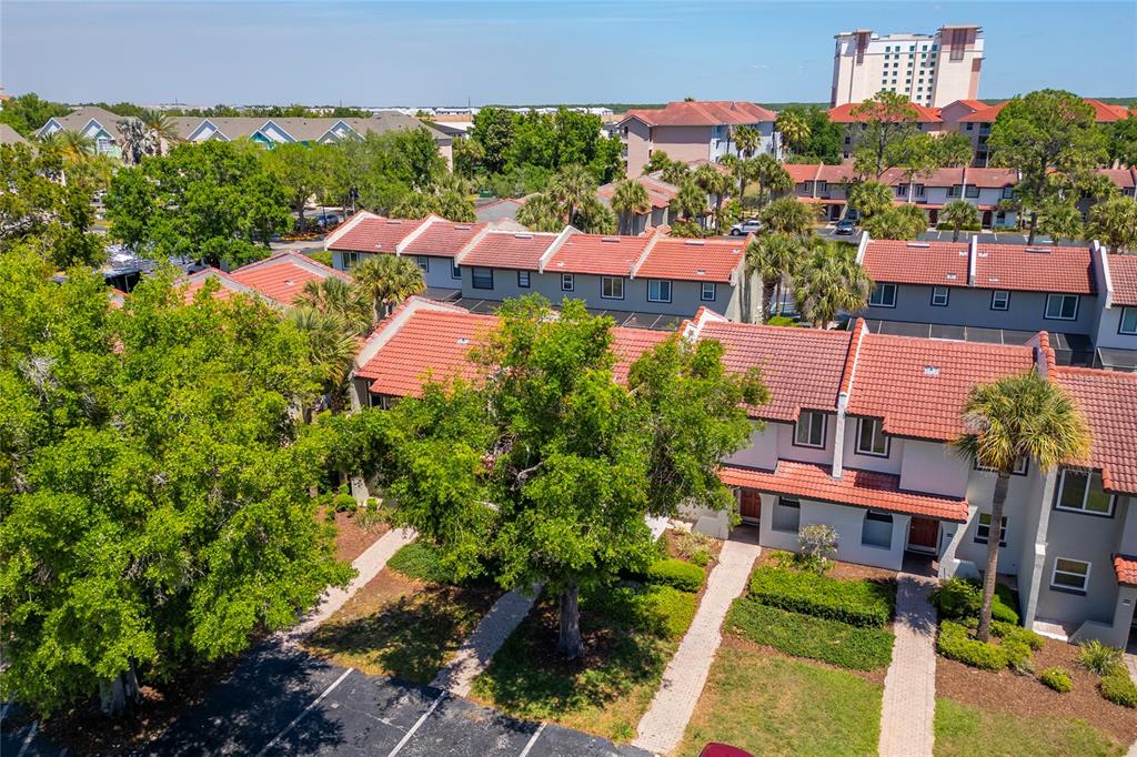 An aerial view shows multi-story townhomes with red tile roofs and surrounding trees and parking — 3118 MAGIC KINGDOM COURT, KISSIMMEE, FL